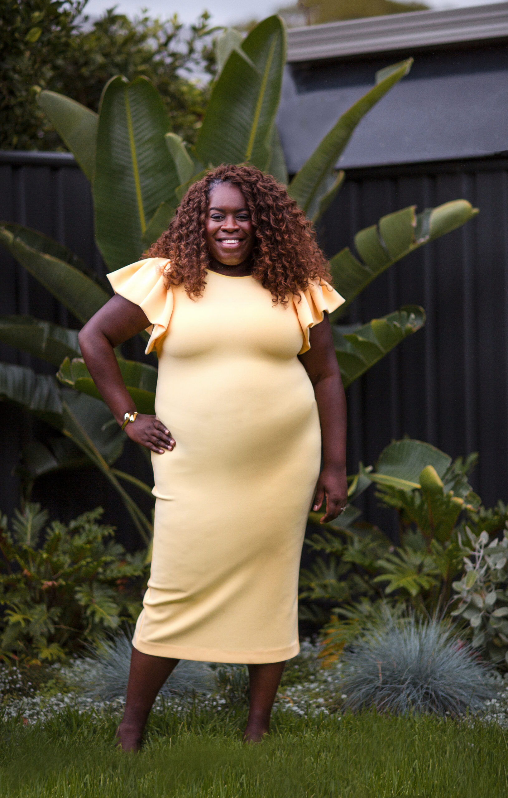 Alisha Waterman standing in her garden in a yellow dress, smiling